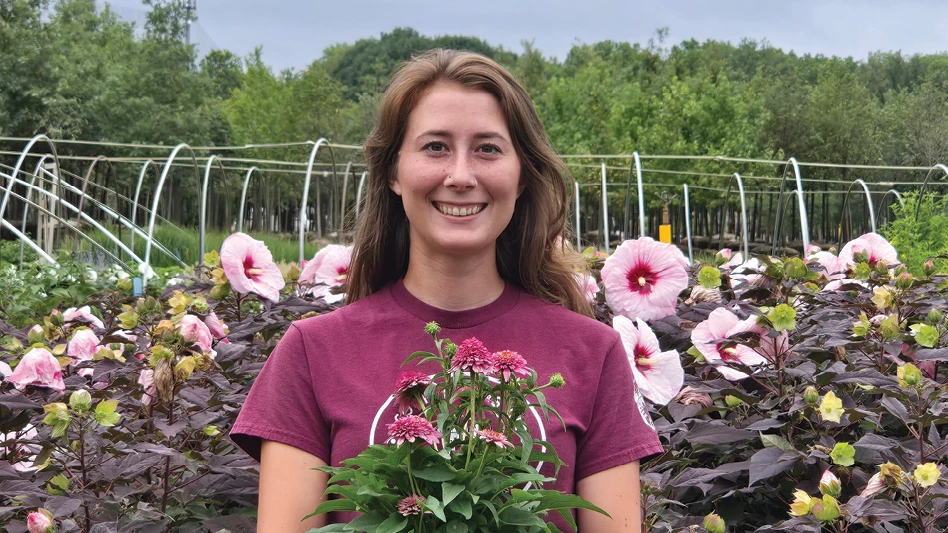 A girl smiling while standing in front of pink and purple hibiscus.